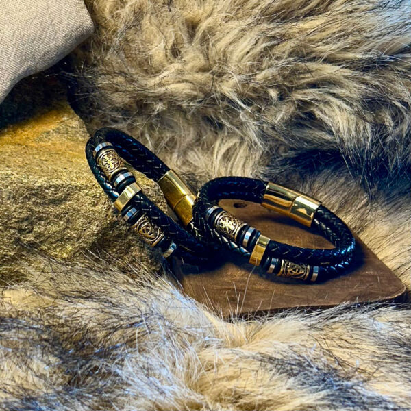 Svart läderarmband med symboler i rostfritt stål och mässing liggandes på trä med päls runtom