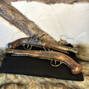 Två dekorativa flintlåspistoler i mörkt trä med mässingsdetaljer, liggande på svart tyg och fäll mot rustik vägg