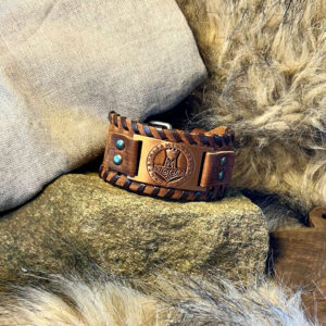 Armband i brunt läder med tors hammare-symbol liggandes på en sten med päls runtom