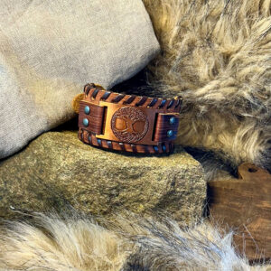 Armband i brunt läder med Yggdrasil-symbol liggandes på en sten med päls runtom