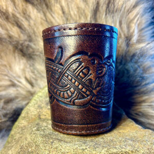 Tärningskopp i brunt präglat läder ståendes på en skiva av trä med päls omkring