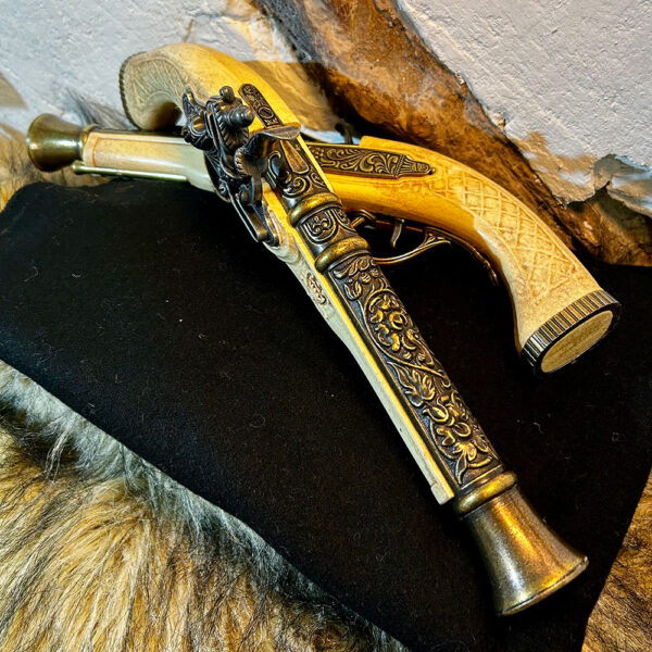 Två dekorativa flintlåspistoler i elfenbensimitation med detaljerade metallbeslag, liggande på svart tyg och fäll